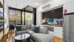 A modern kitchen with a stainless steel refrigerator, a dining area with a table and chairs, and a living room with a sectional sofa and a coffee table. - 1-bed Unit With Alfresco Dining and BBQ (Sydney)
