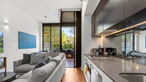A modern kitchen with a built-in oven and a large sink. There is a grey sofa with cushions in the living area. - 1-bed Unit With Alfresco Dining and BBQ (Sydney)