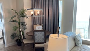 Un salon moderne avec un canapé, une table avec une lampe, un coin repas avec des chaises, une plante en pot et une vue sur l’extérieur.