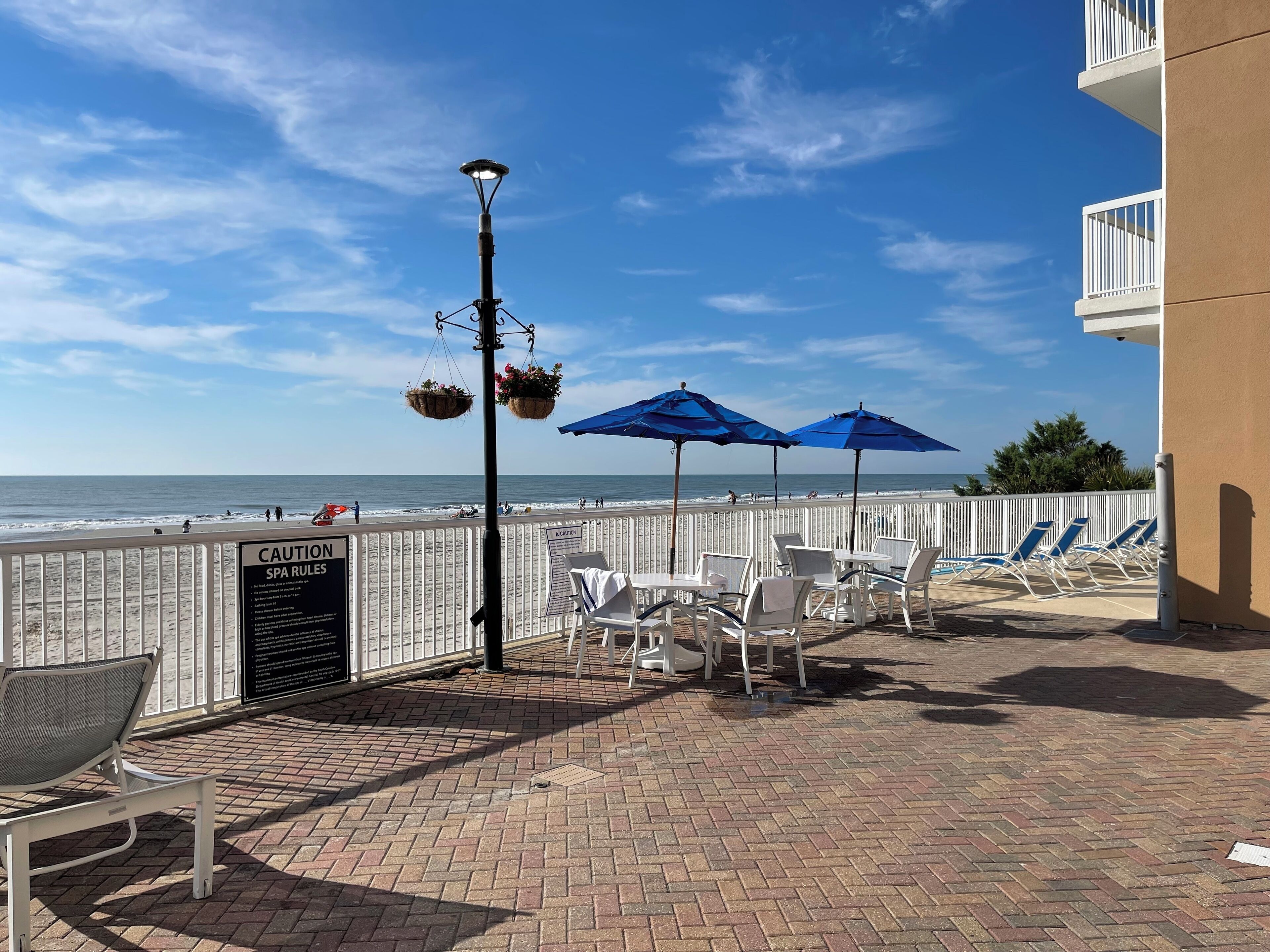 Eine Terrasse direkt am Strand mit weißen Stühlen und blauen Sonnenschirmen, mit Blick auf den Ozean.