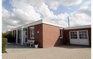 A single-story brick building with a white door, a bench, and a potted plant outside. - Strandnaher Bungalow Renoviert, Dornumersiel (Dornum)