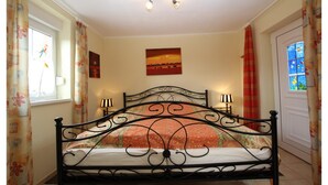 Un dormitorio con una cama, dos lámparas de noche, una ventana con cortinas, un cuadro en la pared y una puerta con ventanal.