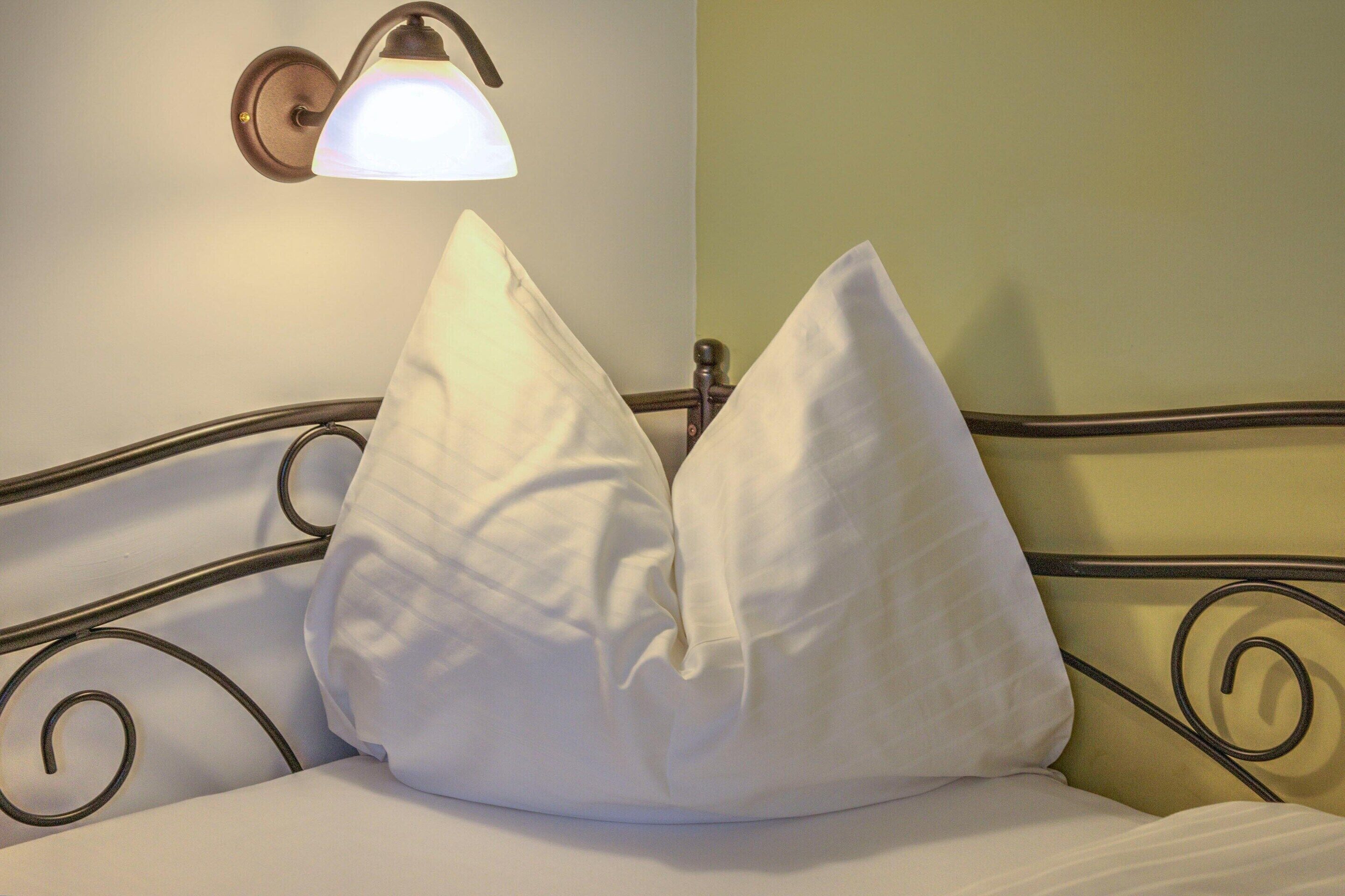 A bed with white bedding and two white pillows, a wall-mounted light fixture, and a metal headboard with a curved design.