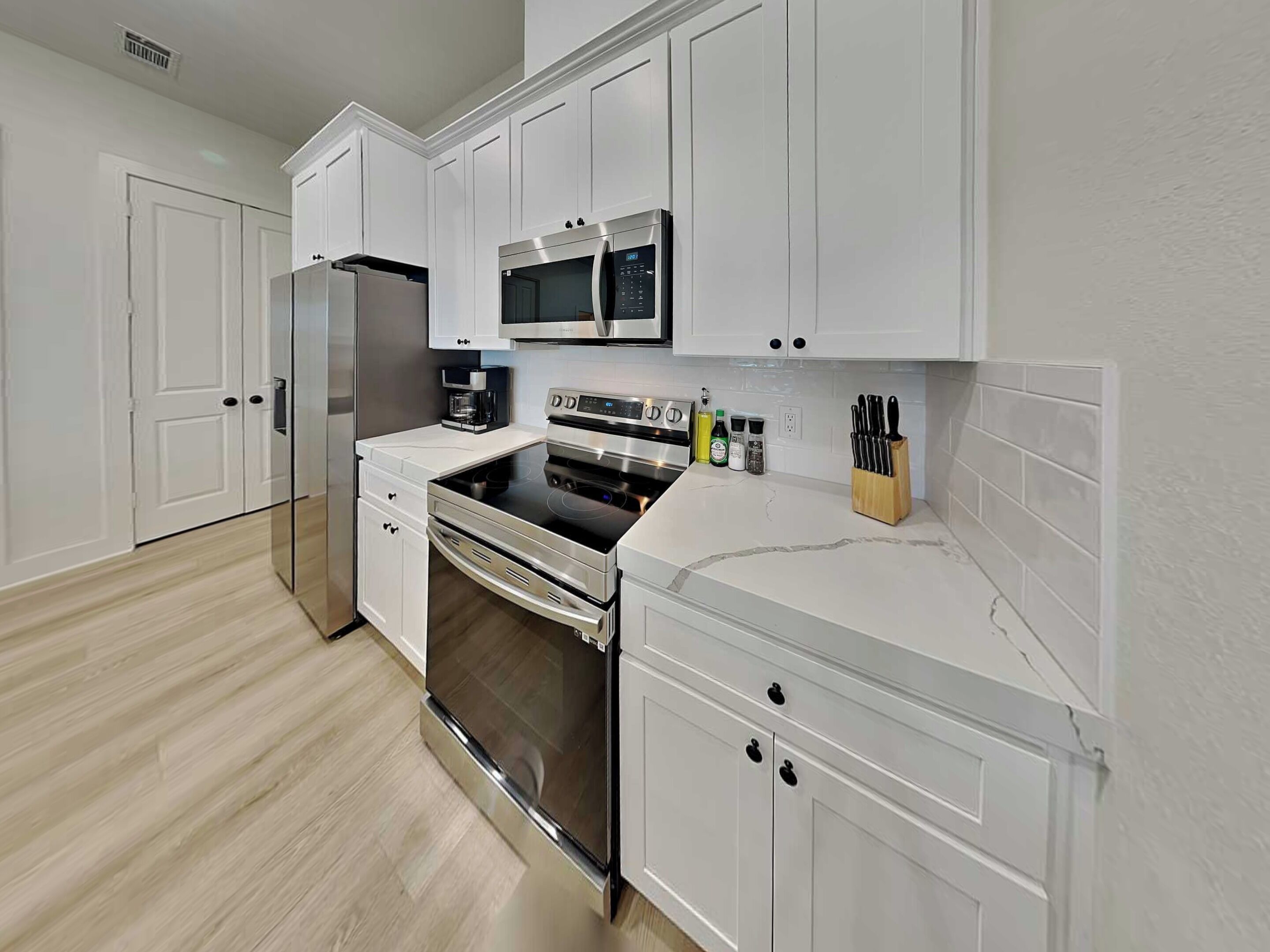 A modern kitchen with white cabinetry, stainless steel appliances, and a marble countertop.