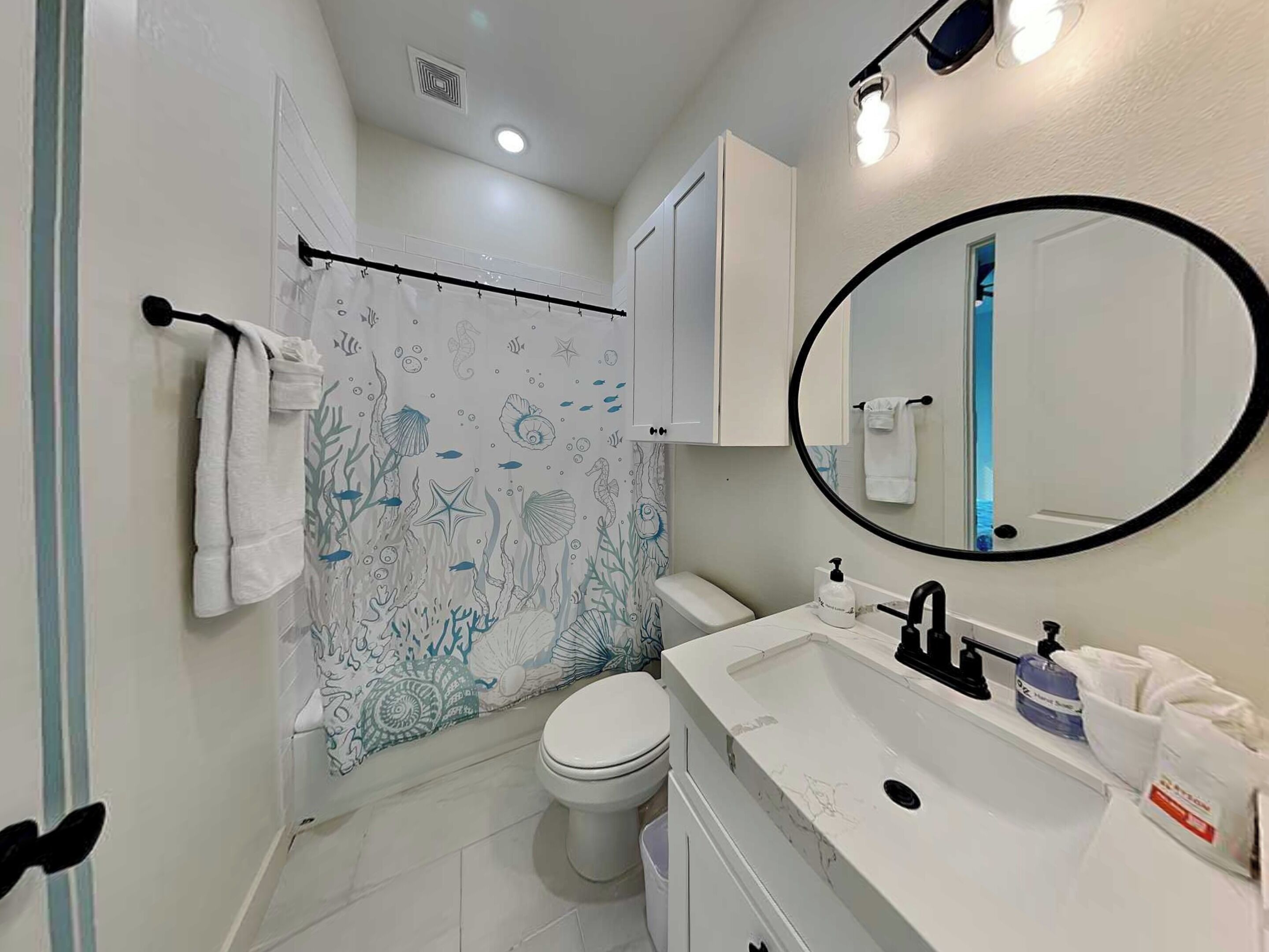 A bathroom with a toilet, sink, mirror, and shower curtain with an underwater theme.