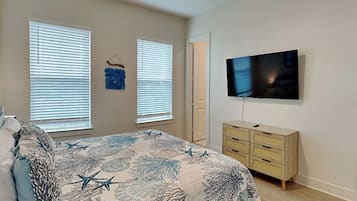 A bedroom with a bed, two windows with blinds, a dresser, a television, and a ceiling fan.