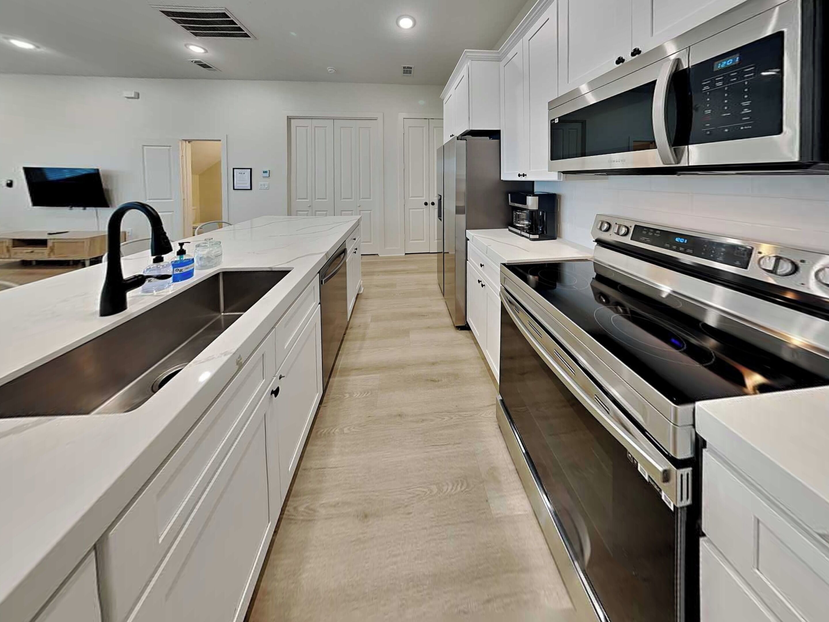 A modern kitchen with white cabinetry, stainless steel appliances, and a large island with a sink.