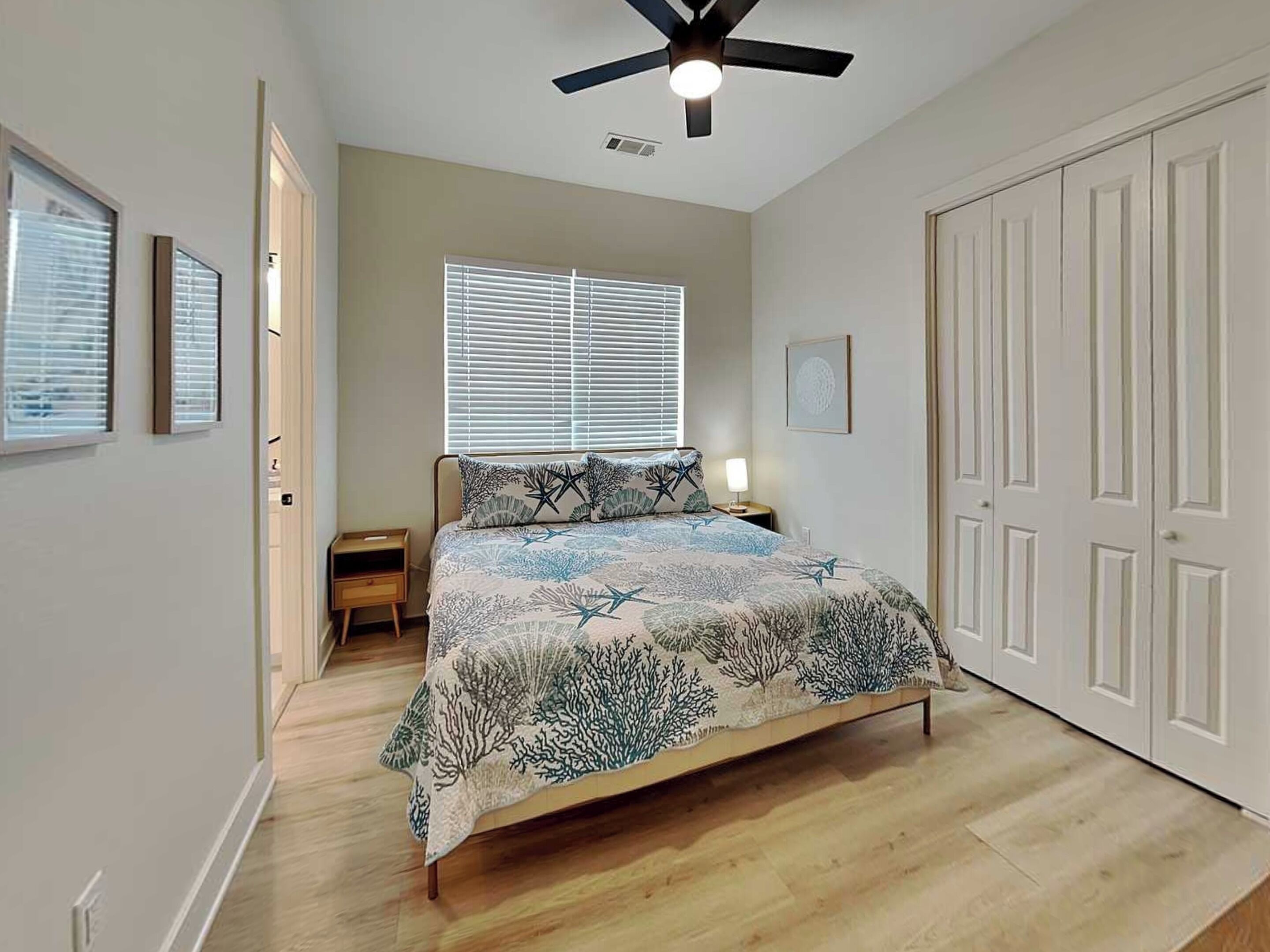 A bedroom with a bed, a ceiling fan, a window with blinds, a nightstand, and a wardrobe.