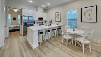 A modern kitchen with white cabinetry, a central island with bar stools, and a dining area with a white table and chairs.