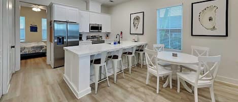 A modern kitchen with white cabinetry, a central island with bar stools, and a dining area with a white table and chairs.