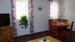 Et værelse med et træbord, stole, et fjernsyn og et vindue med blomstrede gardiner.