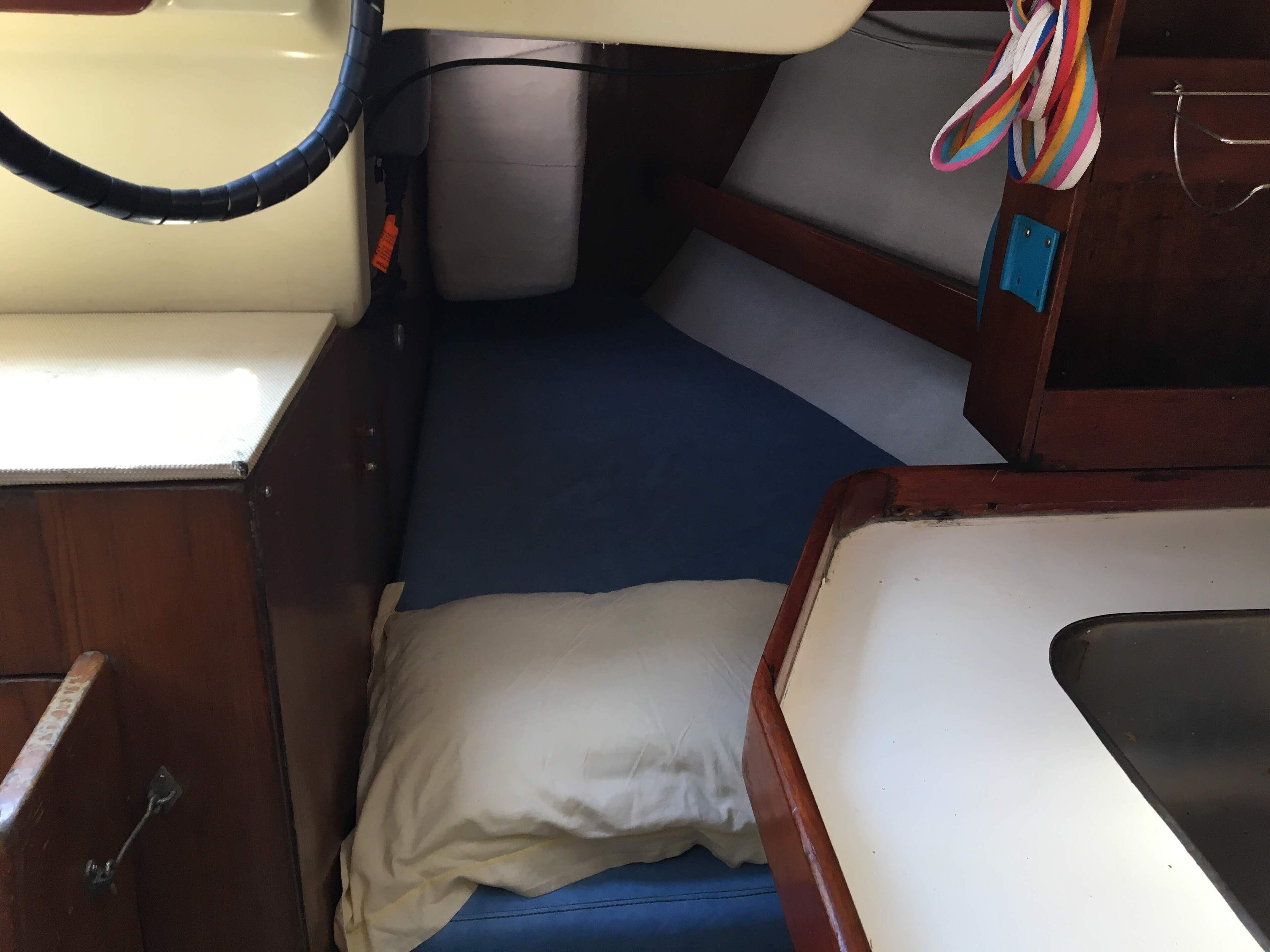 A narrow cabin with a blue cushioned bench, a white pillow, and a small sink.