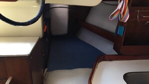 Una cabina stretta con una panca imbottita blu, un cuscino bianco e un piccolo lavandino.