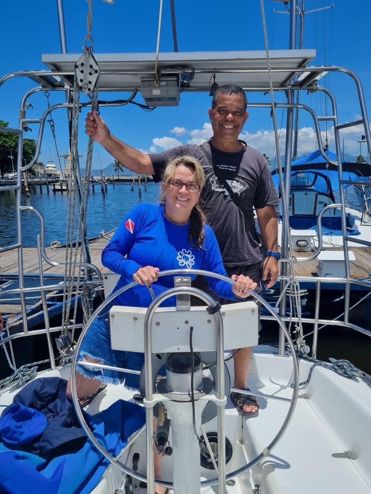 Une personne tient la barre d’un bateau, tandis qu’une autre personne se tient derrière elle.