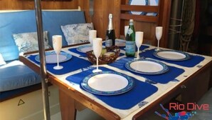 Un tavolo imbandito con piatti, bicchieri e una bottiglia, in una stanza dalle pareti in legno e una panca imbottita blu.