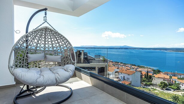 A balcony with a hanging chair, a view of the sea, and a cityscape in the background. - Villa Vista (Crikvenica)