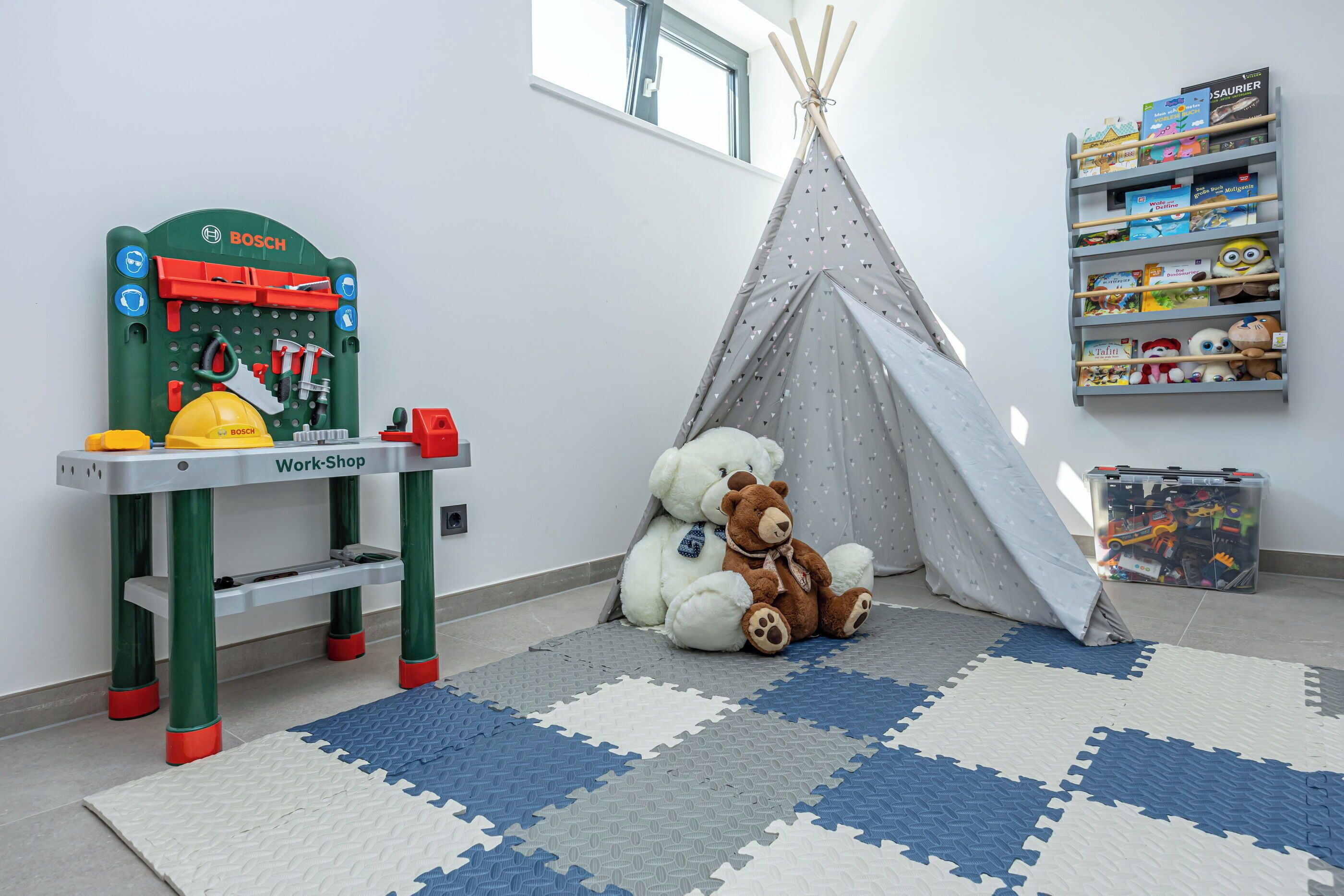 A children's play area with a workbench, a teepee, and a toy storage shelf.