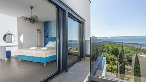 A modern bedroom with a large bed, a glass door leading to a balcony with a city view. - Villa Vista (Crikvenica)