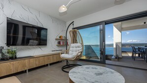 A modern living room with a TV, bookshelves, a hanging chair, and a view of the sea. - Villa Vista (Crikvenica)