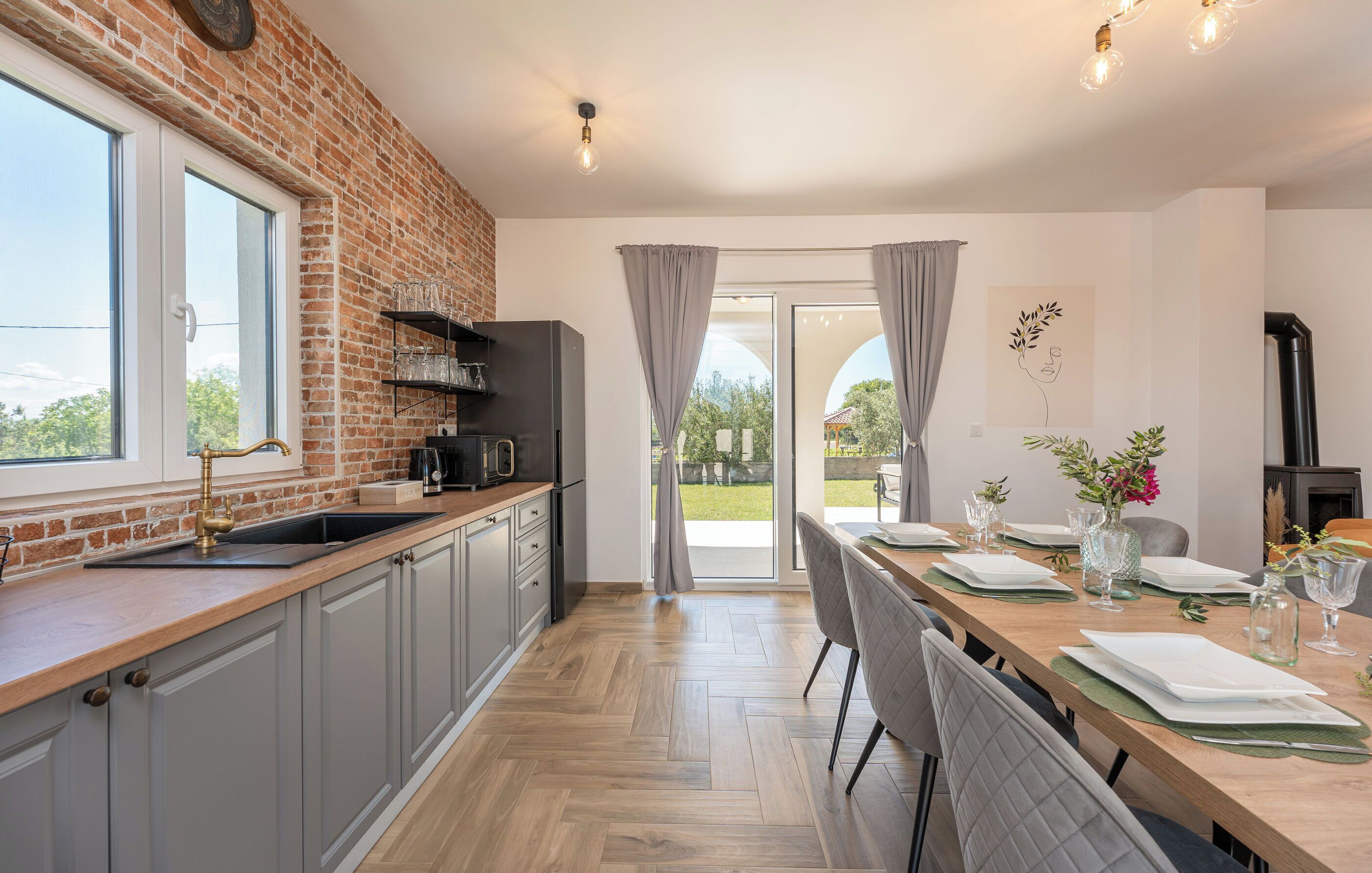 A kitchen with a brick wall, a sink, a refrigerator, and a dining area with a table set for two.