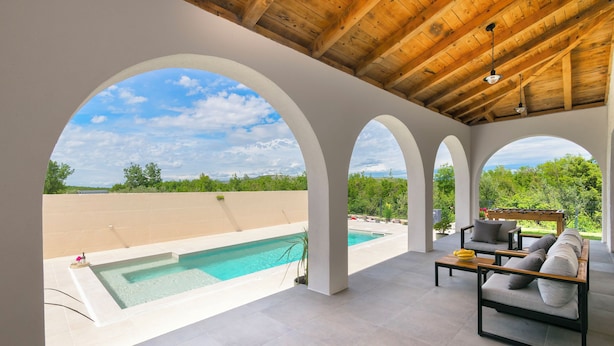 A covered outdoor area with a pool, seating, and a view of greenery. - Villa Olivarum (Stankovci)