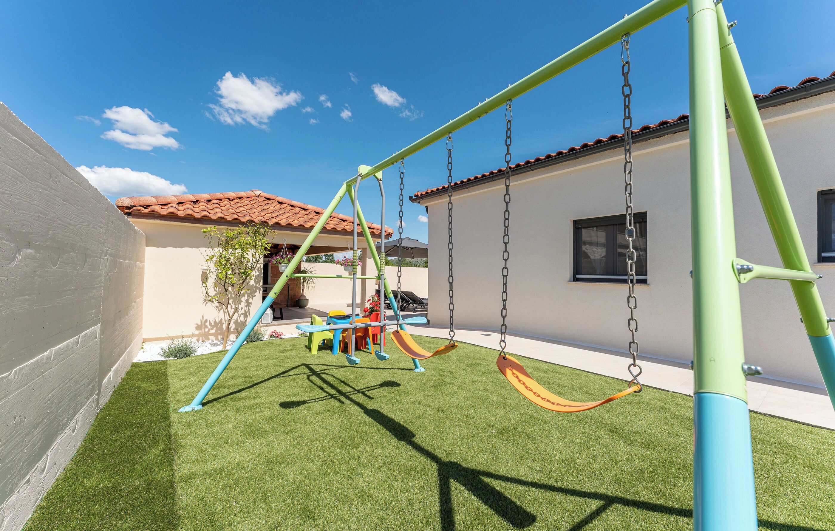 A playground with swings and slides, a small tree, and a building with a tiled roof.