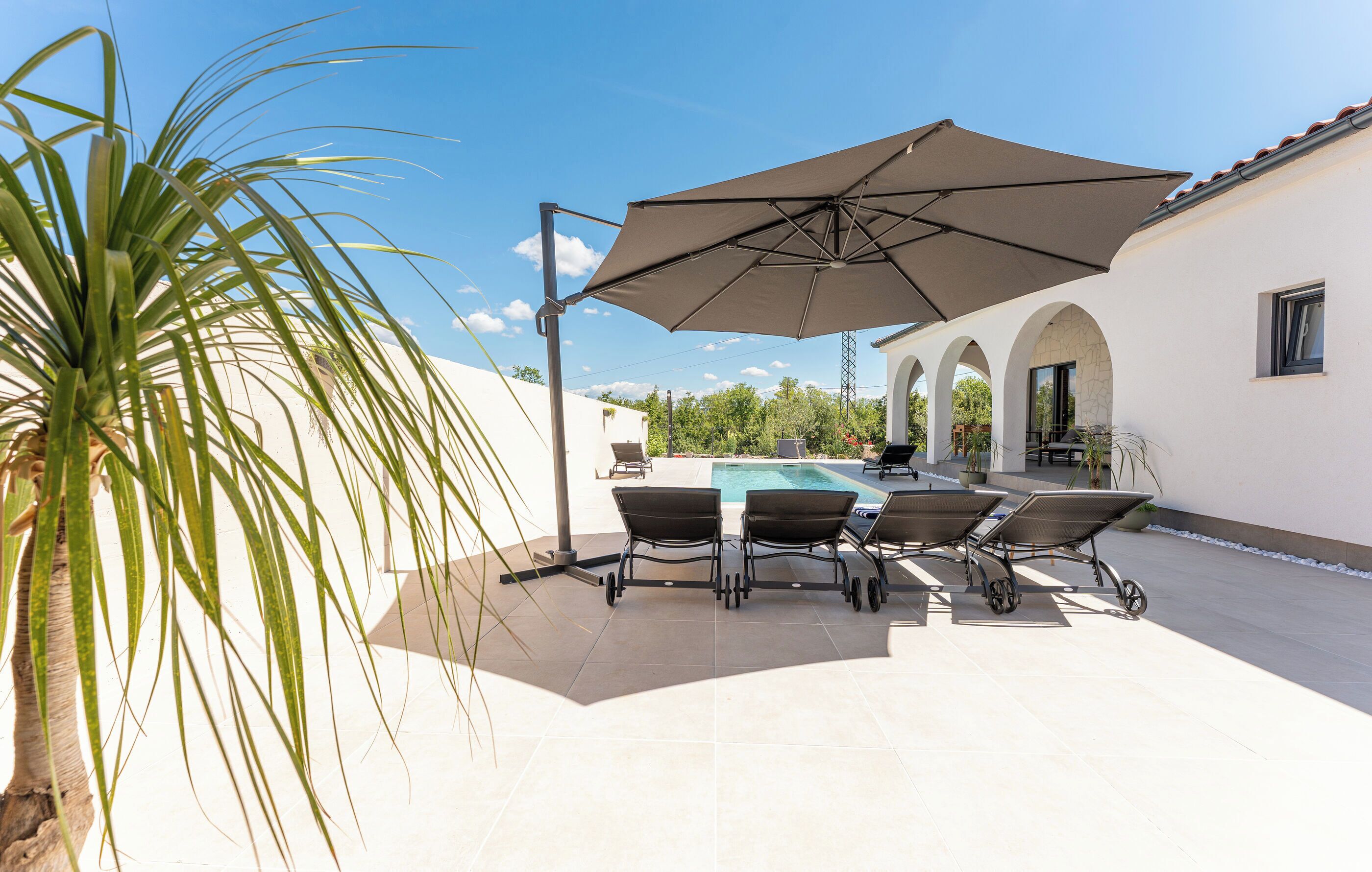 Een zwembadterras met een tafel, stoelen en een grote parasol.