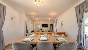 A dining area with a wooden table set for four, grey upholstered chairs, and a modern chandelier. - Villa Olivarum (Stankovci)