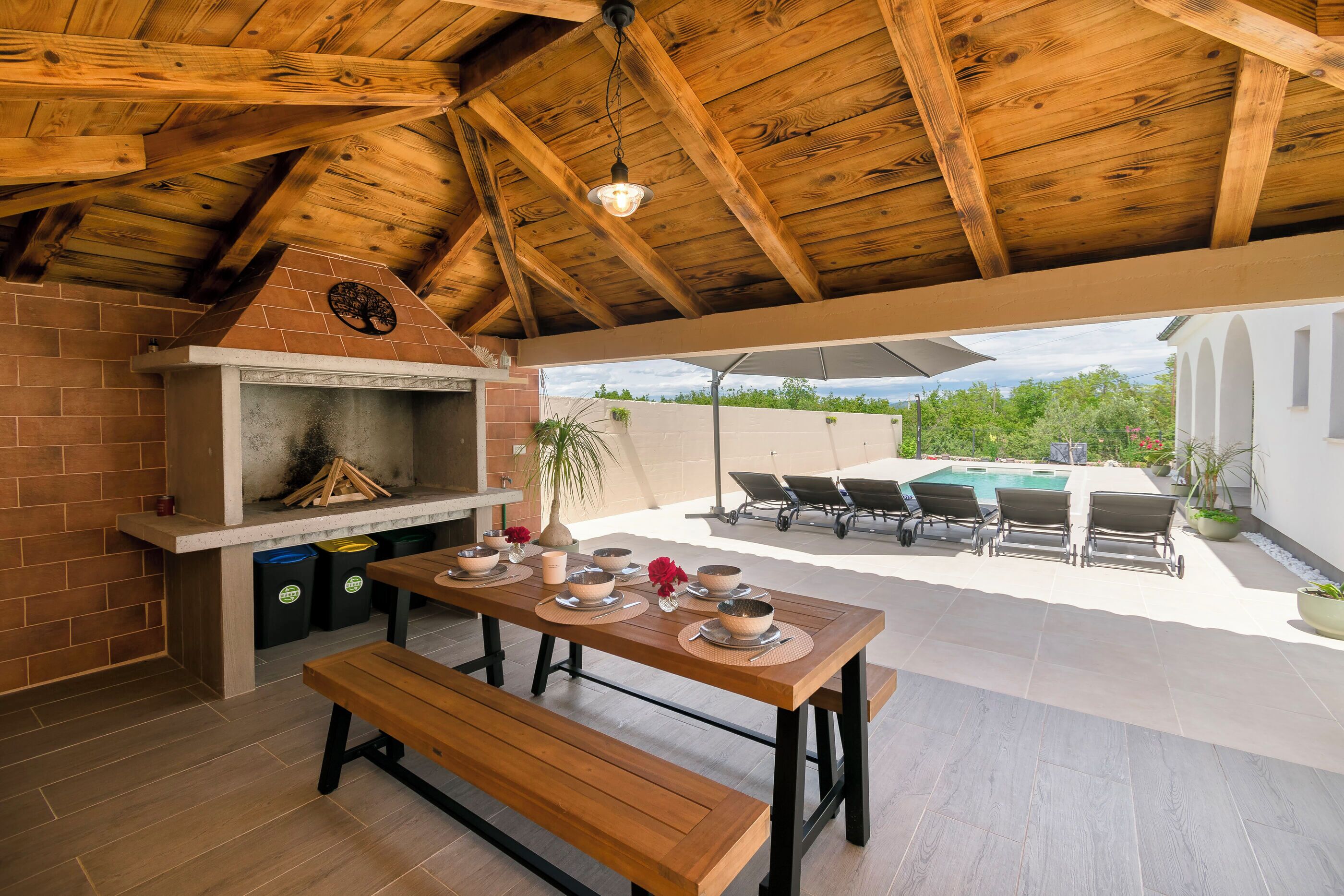 An outdoor patio with a wooden table, benches, and a barbecue grill.