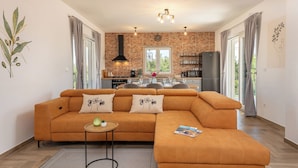 A modern living room with a large orange sofa, a small round table, and a kitchen in the background. - Villa Olivarum (Stankovci)