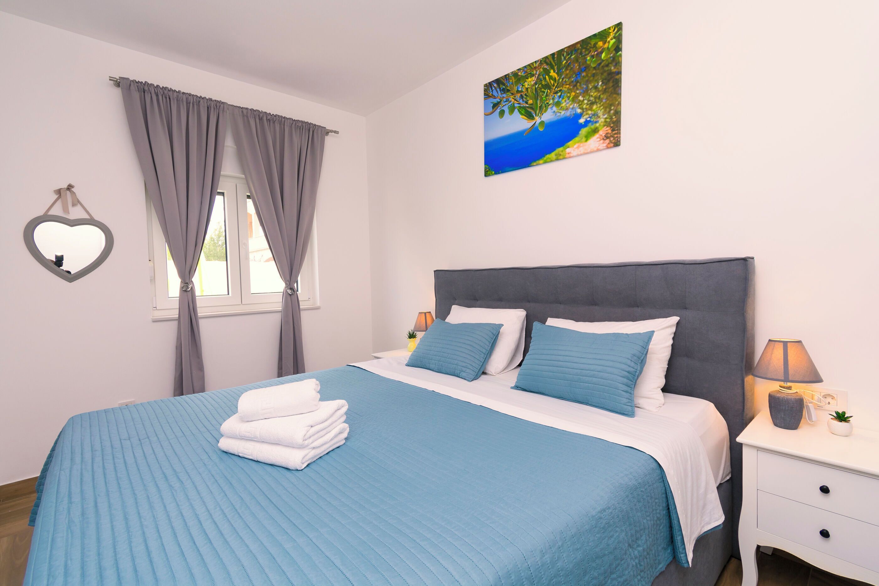 A neatly made bed with a blue bedspread, a white pillow, and a grey headboard.