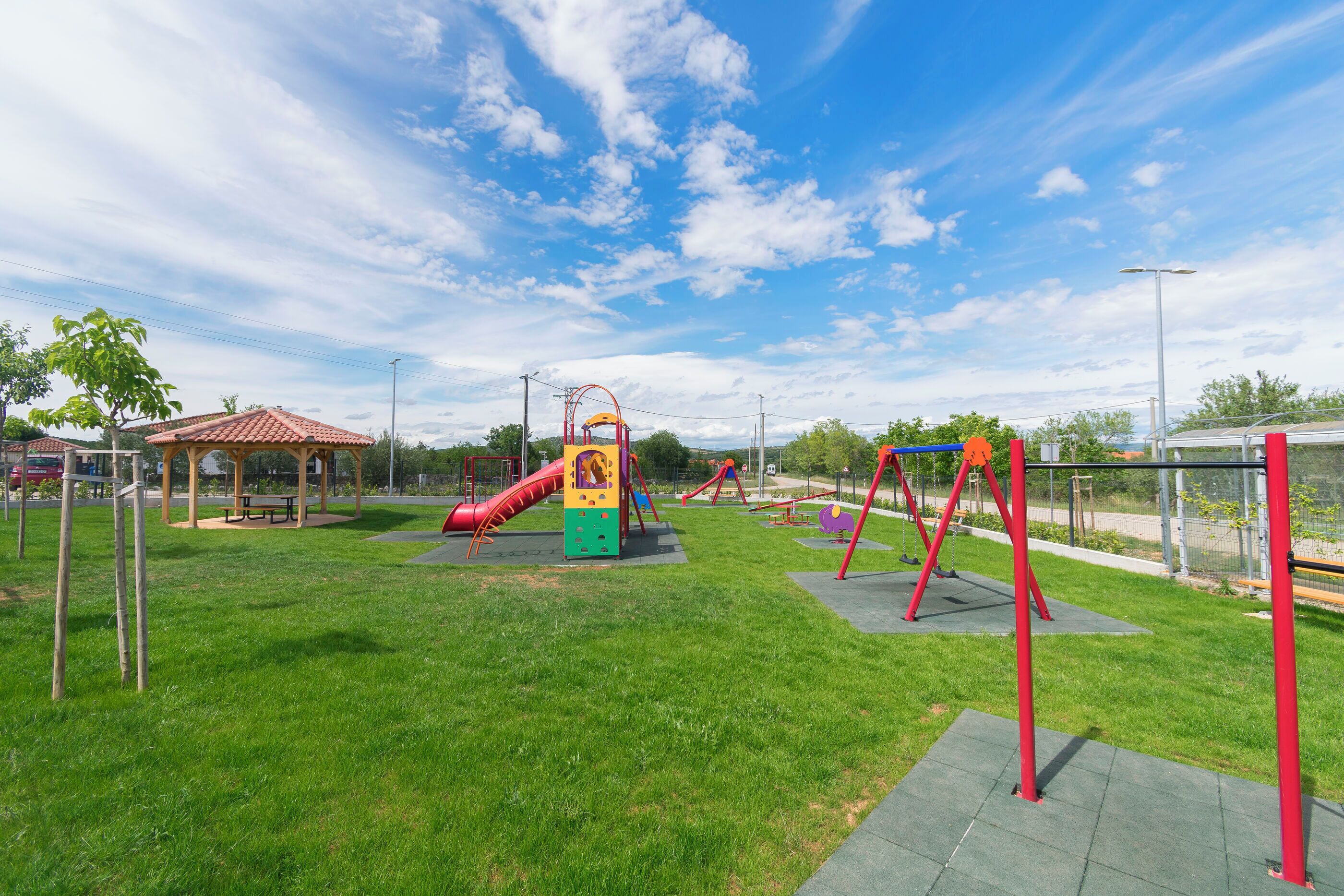 Un parque infantil con toboganes y columpios, una mesa de picnic y una zona vallada.