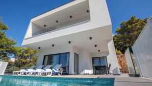 Ein modernes, zweistöckiges Haus mit Swimmingpool, Liegestühlen und Essbereich.
