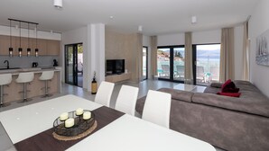 Ein modernes Wohnzimmer mit Sofa, Esstisch und Küchenbereich mit Barhocker.