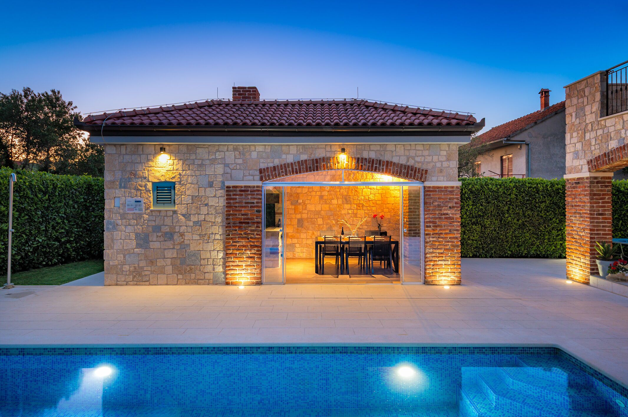 A stone building with a tiled roof, a glass enclosure, and a pool in front.