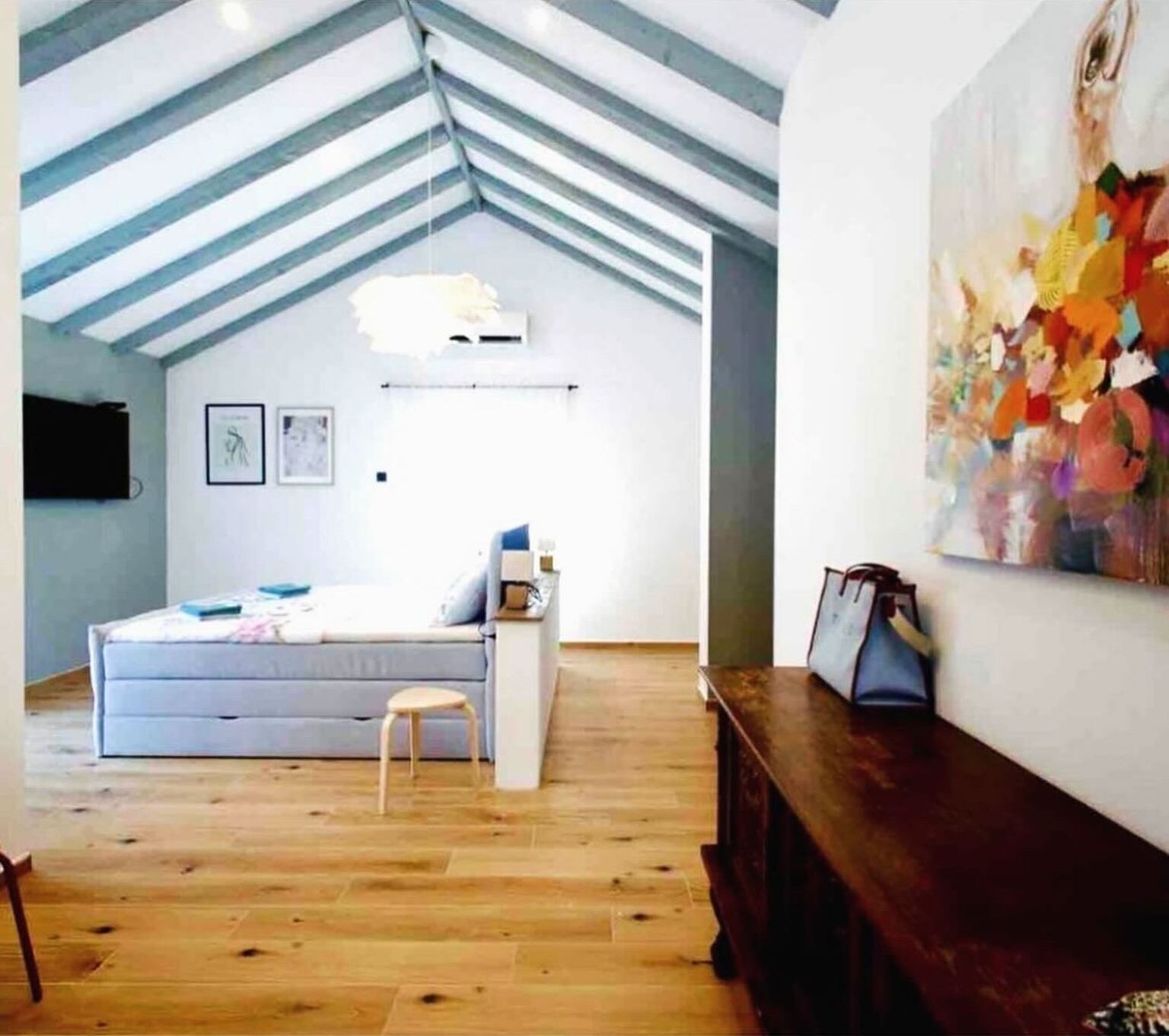 A loft-style bedroom with a sloped ceiling, a bed, a desk, and a large abstract painting.