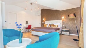 A modern bedroom with a large bed, two blue armchairs, a white side table, and a vase of flowers. - Villa Roko (Malinska-Dubasnica)
