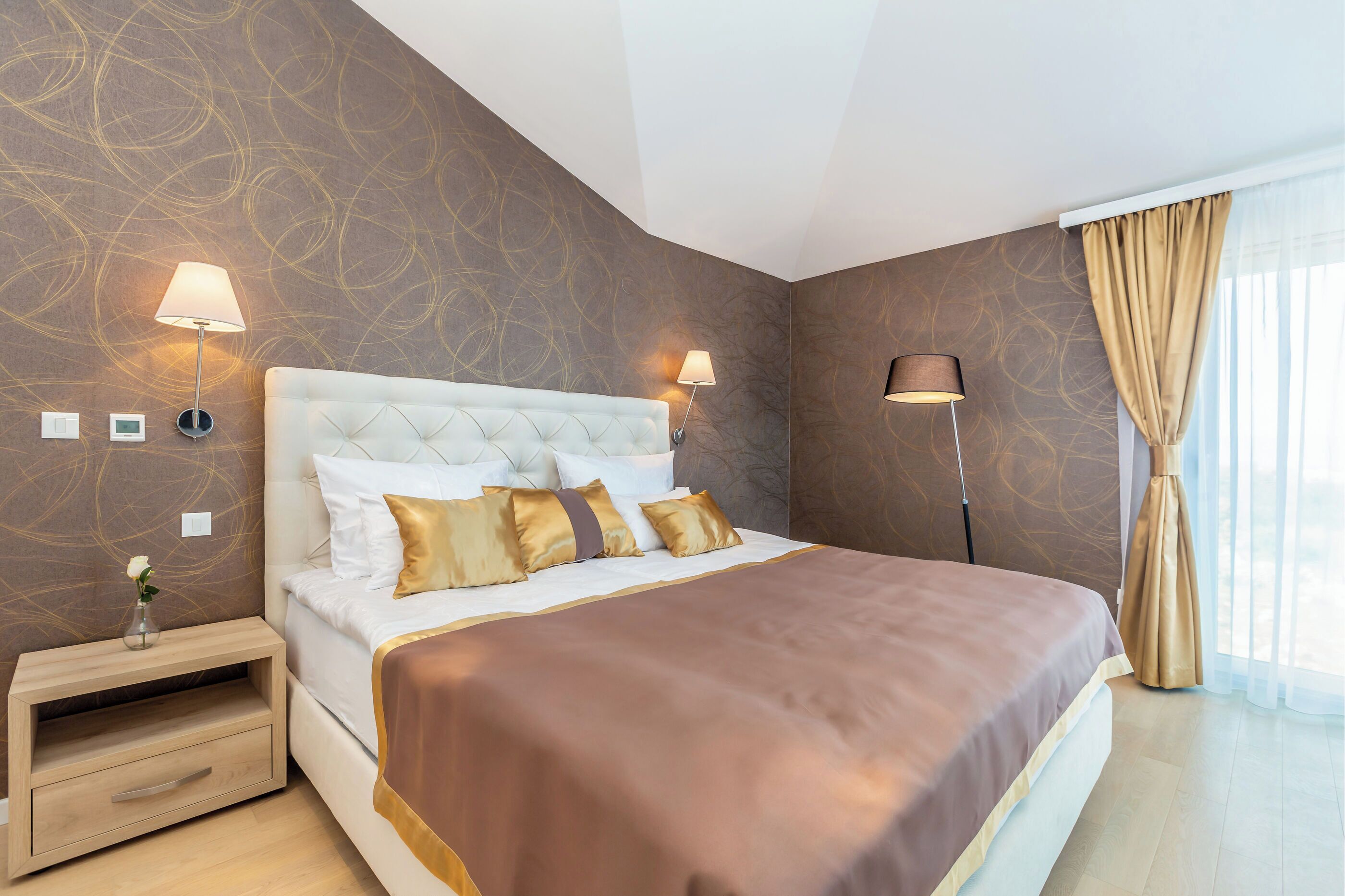 A neatly arranged bedroom with a large bed, two bedside lamps, and a nightstand with a drawer.