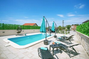 Una piscina con lettini e ombrelloni, circondata da un muro in pietra e vegetazione.