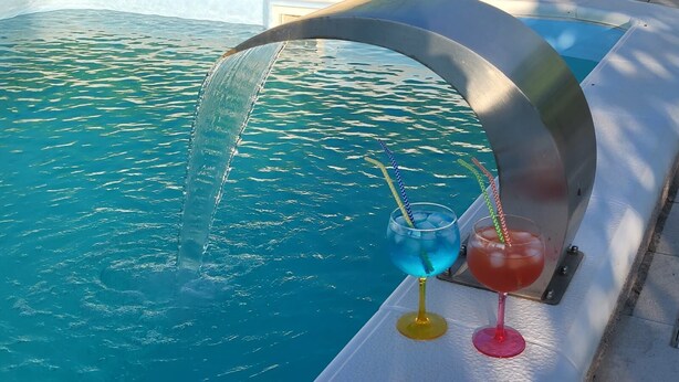 Ein Pool mit Wasserspiel und zwei Getränken auf einem Tisch.