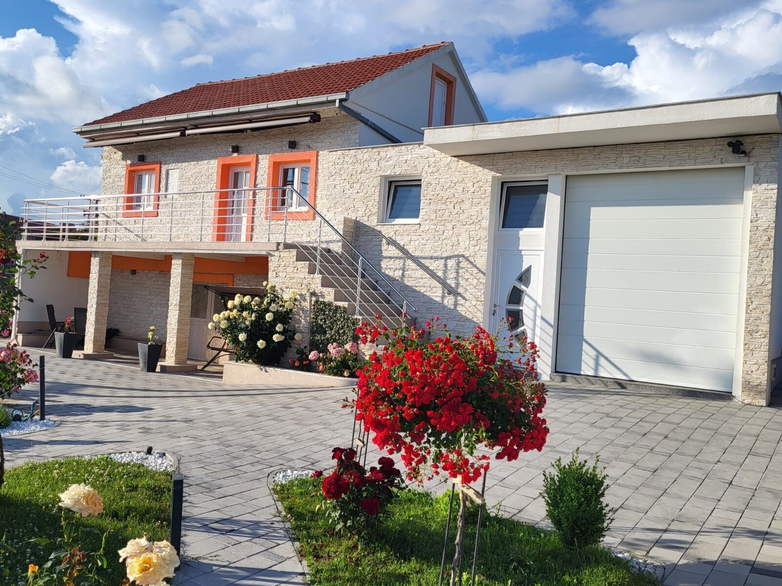 A two-story house with a stone facade, orange-framed windows, and a red-tiled roof.