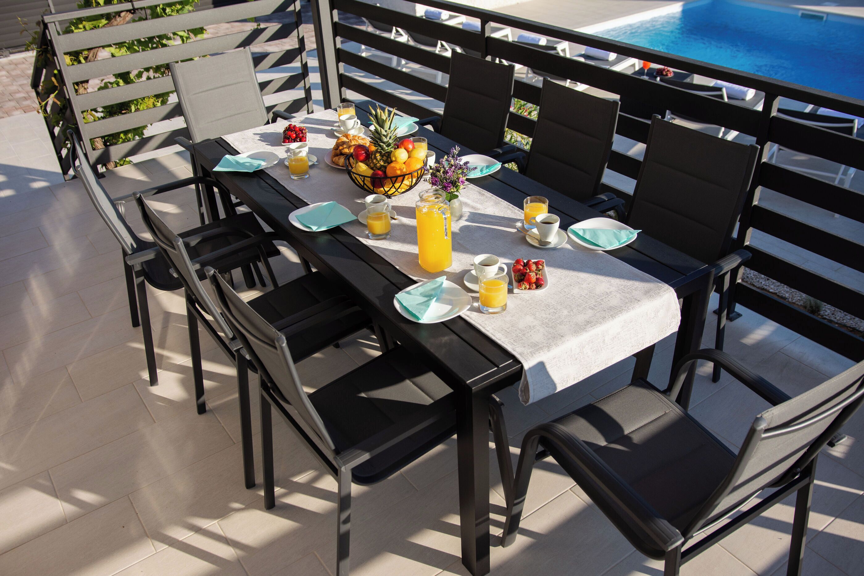 A dining table set for four with chairs, a fruit bowl, and a pool in the background.