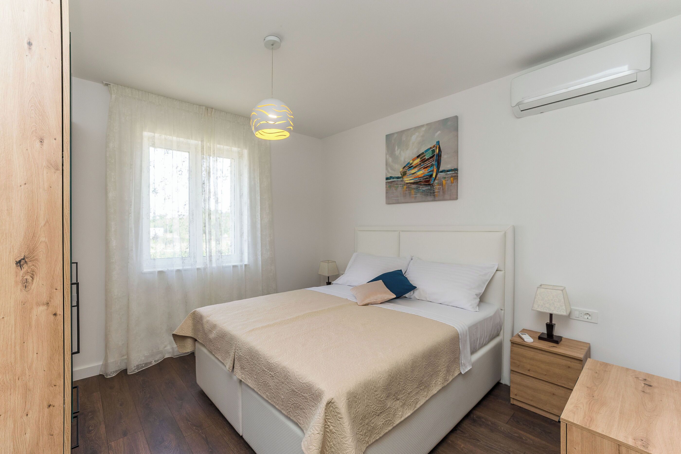 A bedroom with a bed, bedside tables, a lamp, a painting, and a window with curtains.