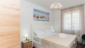 A neatly arranged bedroom with a bed, bedside table, lamp, and a painting of a lighthouse. - Villa Residence Sunrise (Privlaka)