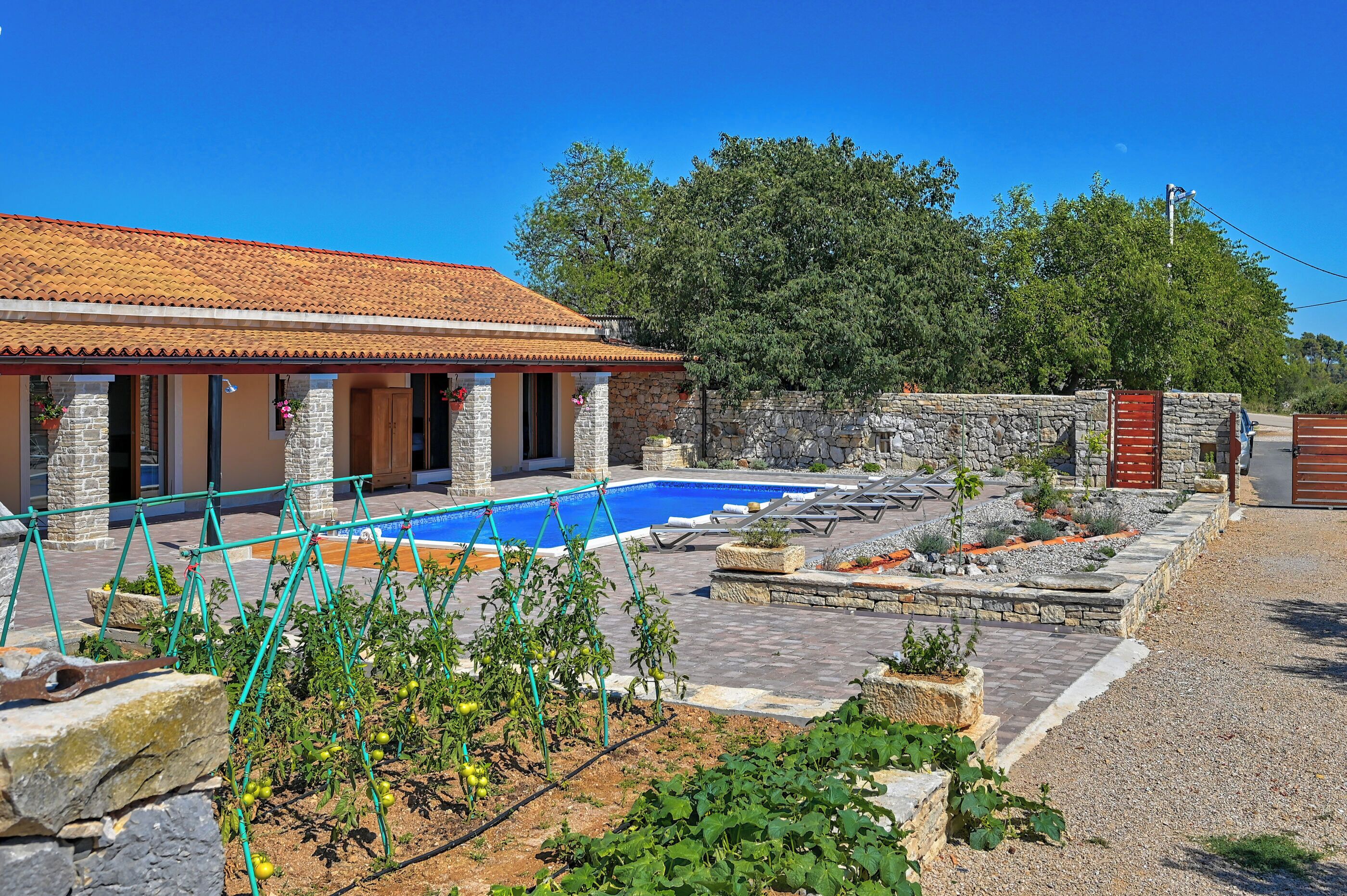 Ein Haus mit Swimmingpool, Steinmauern und einem Garten mit Tomatenpflanzen.