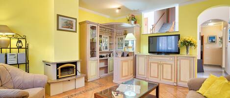 Un salon comprenant un canapé, une table basse, une cheminée, un téléviseur et un coin cuisine avec des placards et une cuisinière.