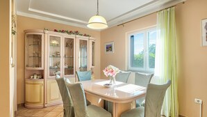 Zona pranzo con tavolo, sedie, un armadietto e una finestra con tende.