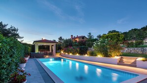 Una piscina rettangolare con bordo piastrellato, circondata da piante in vaso e un gazebo.