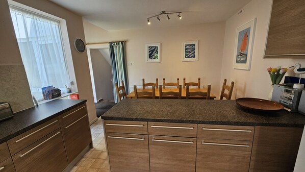 Una cocina con armarios de madera, encimera de granito, una mesa de comedor con sillas y un reloj en la pared.
