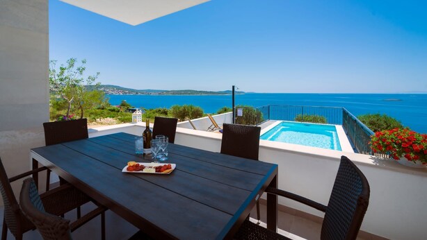 A dining table with chairs and a view of the sea and a swimming pool. - Villa Adio Mare (Rogoznica)